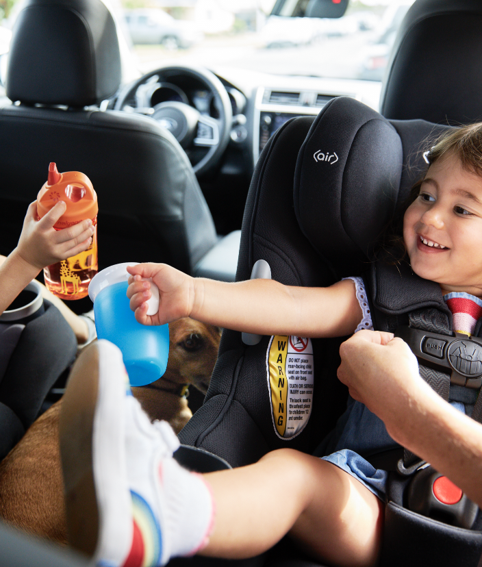Two toddlers sit in carseats in the backseat of a car.