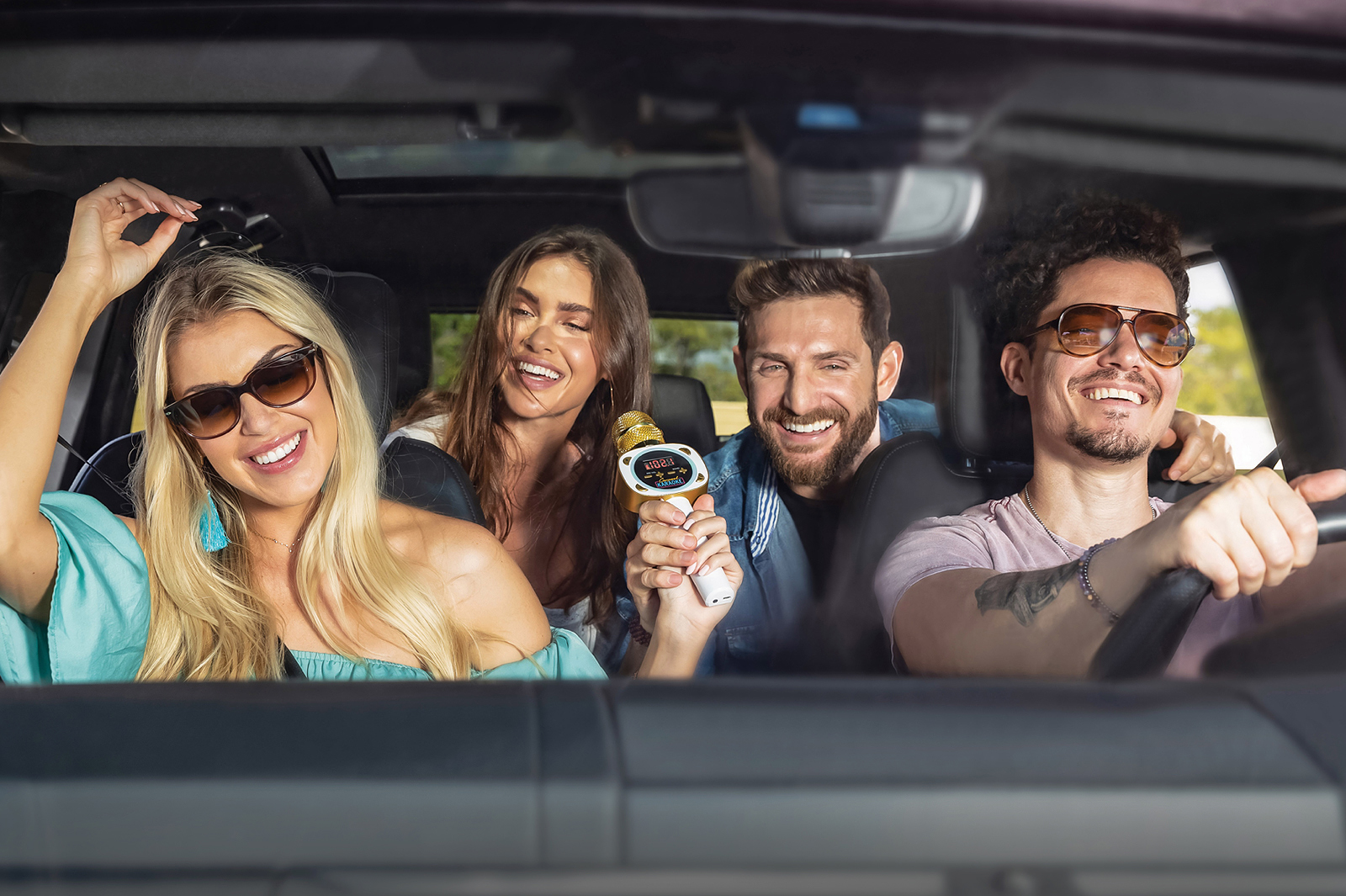 Front view of two men and two women seated in car. All are  smiling, dancing and singing using the Carpool Karaoke product.