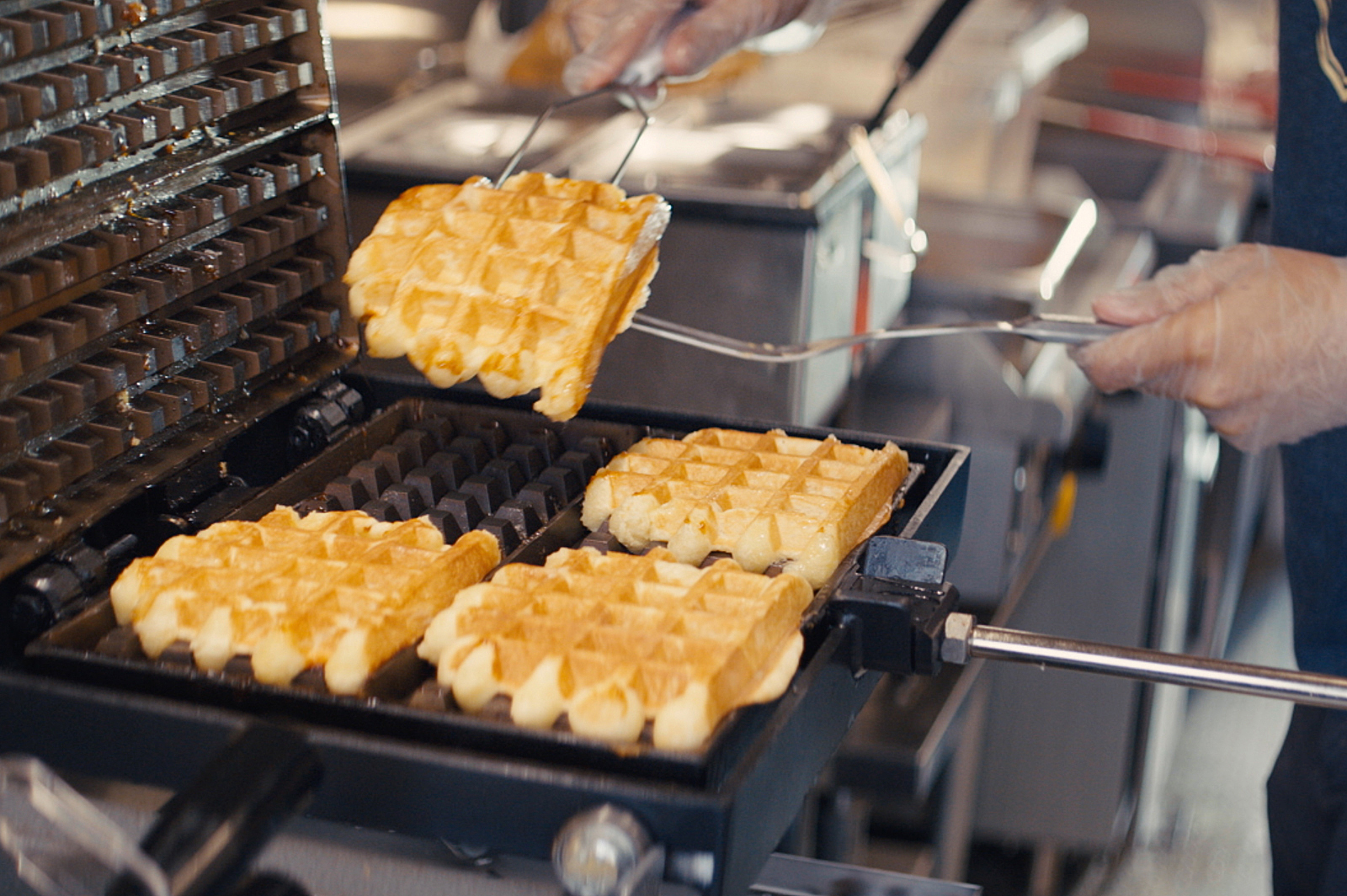 Waffles being flipped in a waffle maker.