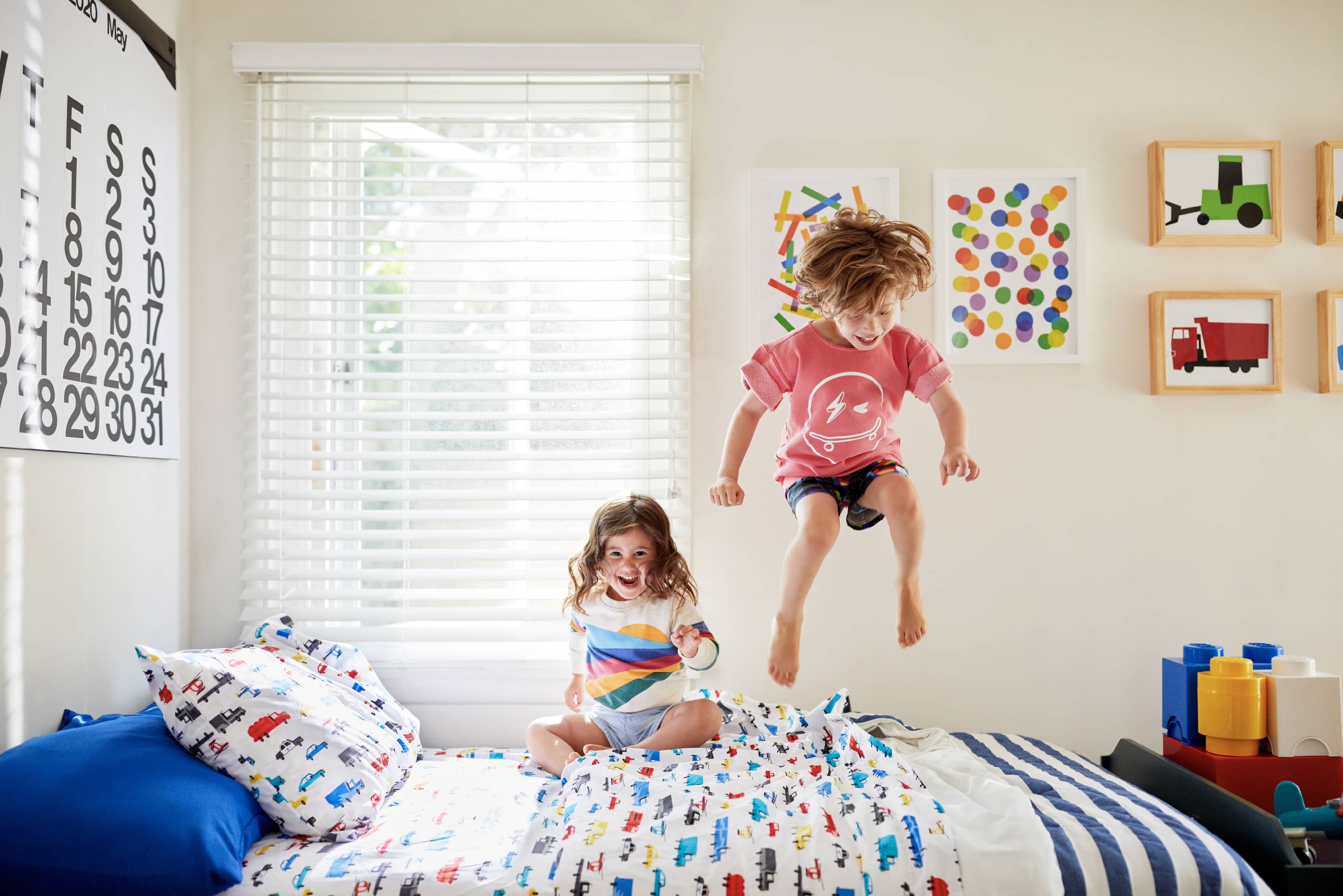 Two children jump on a bed.