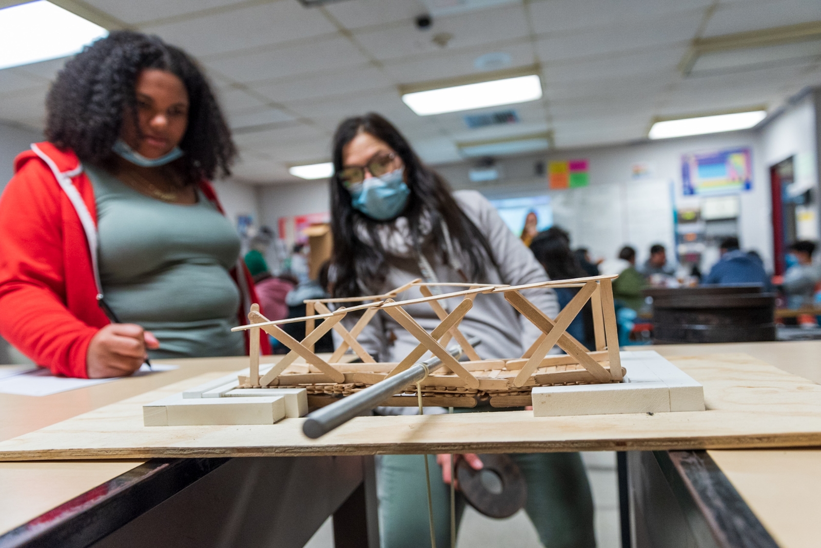 Two students record observations about a bridge made of popsicle sticks.
