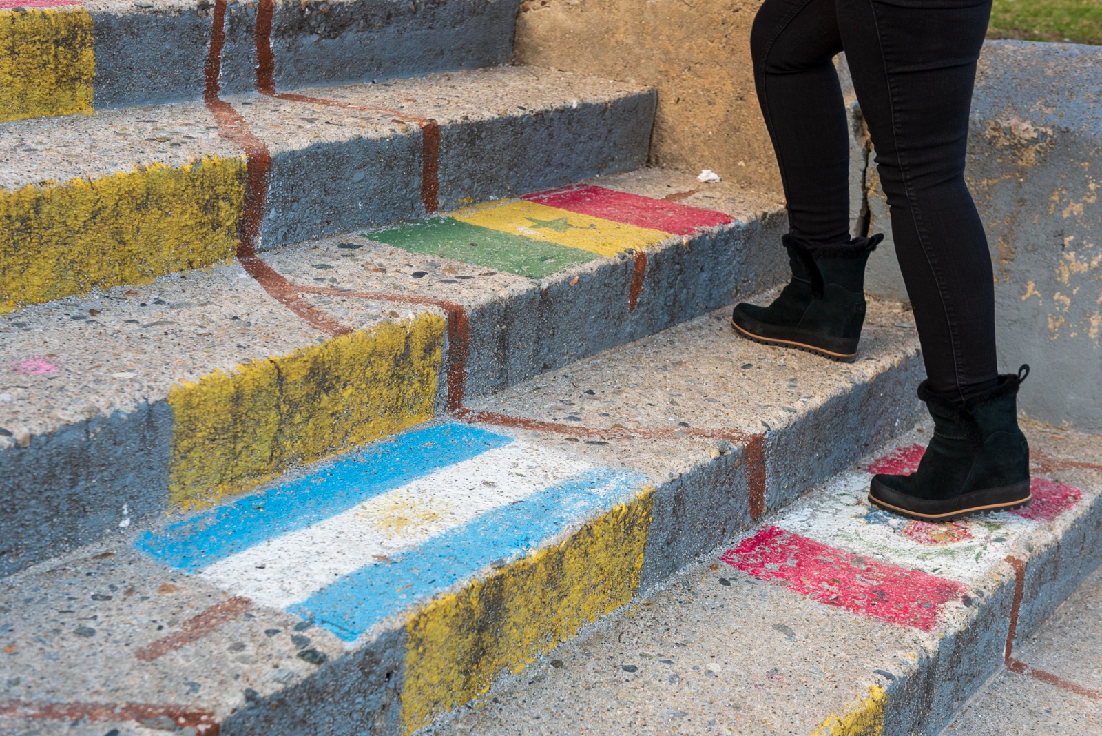 A student walks up a concrete staircase decorated with chalk flags including El Salvador, Senegal, and Peru.