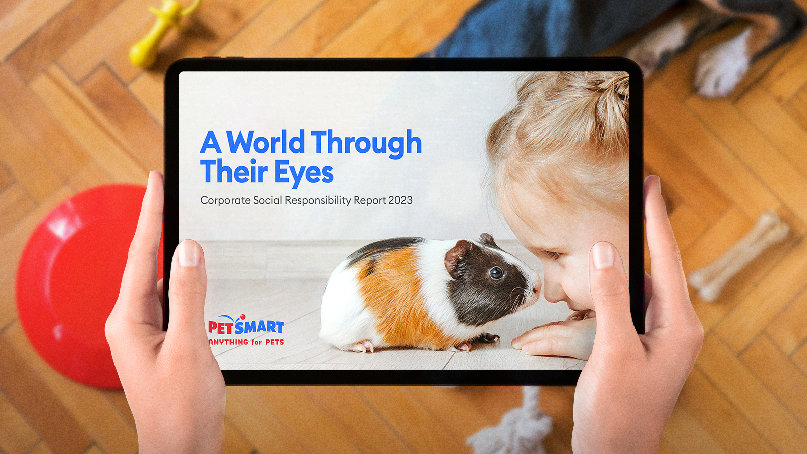 Person holding a tablet displaying PetSmart’s 2023 CSR report cover with a girl and a guinea pig