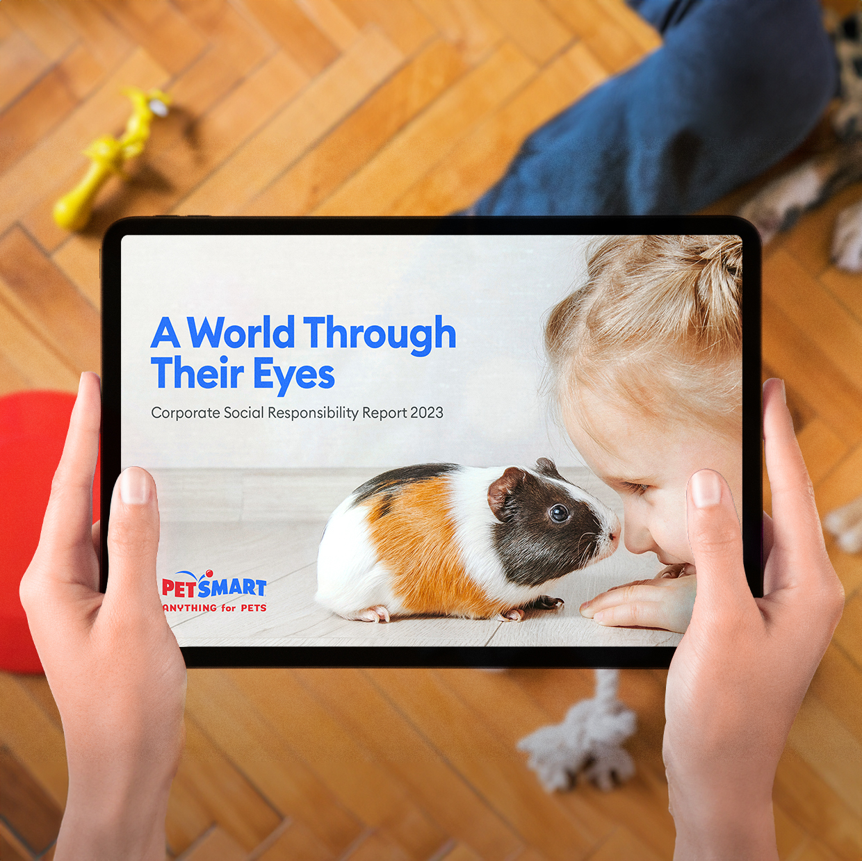 Person holding a tablet displaying PetSmart’s 2023 CSR report cover with a girl and a guinea pig.