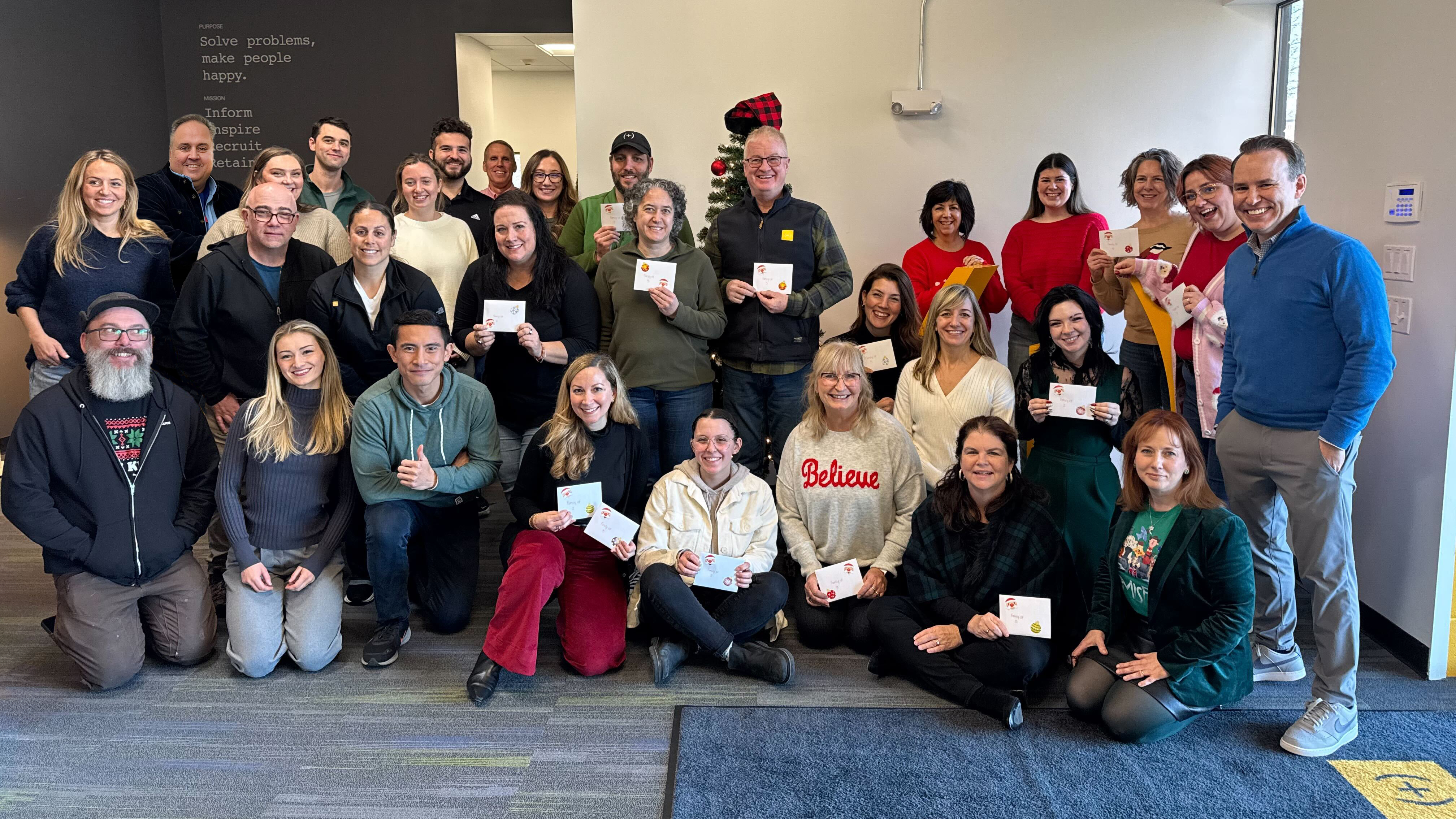 Large group of people smiling and holding cards in an office gather holding holiday cards.